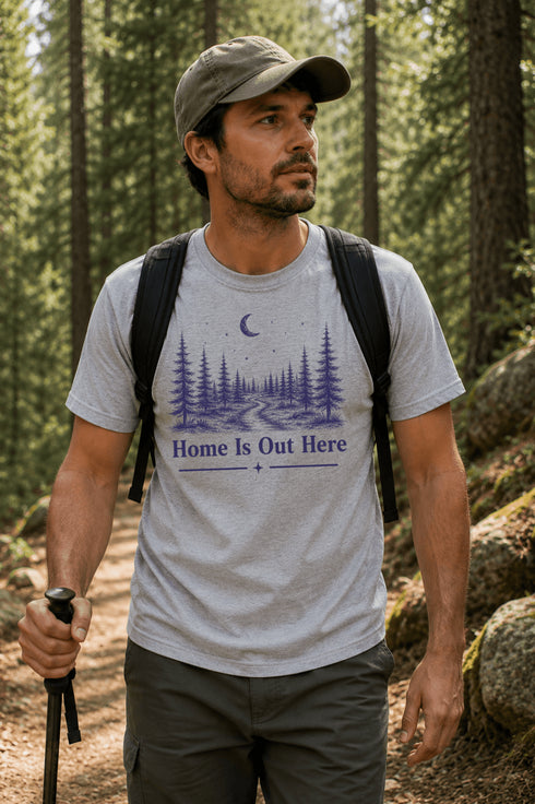 Man hiking in a forest wearing a t-shirt with 'Home is Out Here' design.