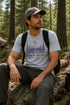 Man sitting on a rock in a forest wearing a t-shirt with a nature-themed design.