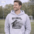 man wearing a grey hoodie with “I Don’t Yell I Coach Loudly” soccer coach design featuring coach pointing on sideline with players in background