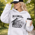 Woman wearing a grey hoodie with “I Don’t Yell I Coach Loudly” soccer coach design featuring coach pointing on sideline with players in background