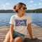 Woman sitting on a dock by a lake wearing a 'It's Lake Time' t-shirt.