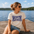 Woman sitting on a dock by a lake wearing a 'It's Lake Time' t-shirt.