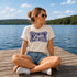 Woman sitting on a dock by a lake wearing a 'It's Lake Time' t-shirt.