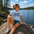 Woman sitting on a rock by a lake wearing a 'It's Lake Time' t-shirt.