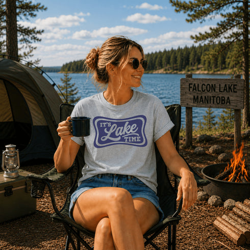 Woman sitting by a campfire at Falcon Lake, Manitoba, holding a mug with 'It's Lake Time' shirt.
