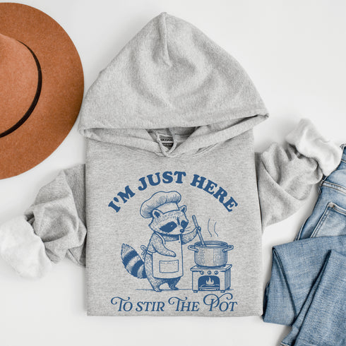 Meet your new favorite hoodie—starring a sarcastic raccoon who’s as skilled at cooking up drama as stirring actual soup.