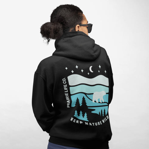 This hoodie features a silhouetted polar bear wandering across layered frozen prairie hills, this design captures the quiet majesty of nature.