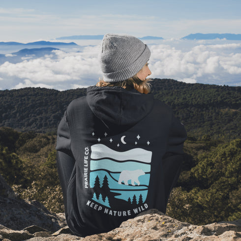 This hoodie features a silhouetted polar bear wandering across layered frozen prairie hills, this design captures the quiet majesty of nature.