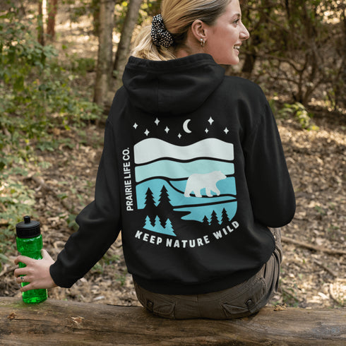 This hoodie features a silhouetted polar bear wandering across layered frozen prairie hills, this design captures the quiet majesty of nature.