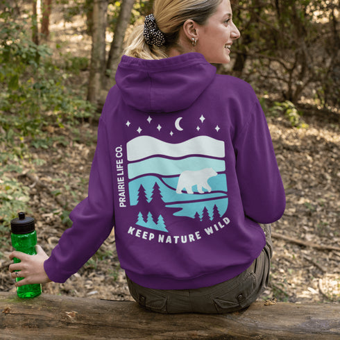 This hoodie features a silhouetted polar bear wandering across layered frozen prairie hills, this design captures the quiet majesty of nature.