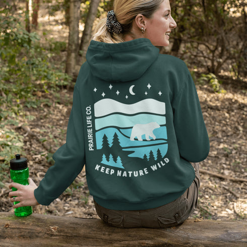 This hoodie features a silhouetted polar bear wandering across layered frozen prairie hills, this design captures the quiet majesty of nature.