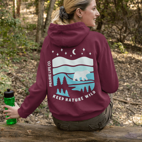 This hoodie features a silhouetted polar bear wandering across layered frozen prairie hills, this design captures the quiet majesty of nature.