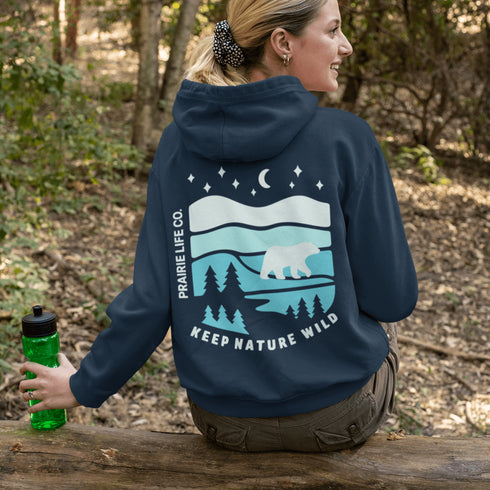 This hoodie features a silhouetted polar bear wandering across layered frozen prairie hills, this design captures the quiet majesty of nature.