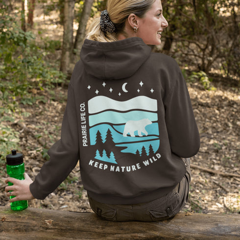 This hoodie features a silhouetted polar bear wandering across layered frozen prairie hills, this design captures the quiet majesty of nature.