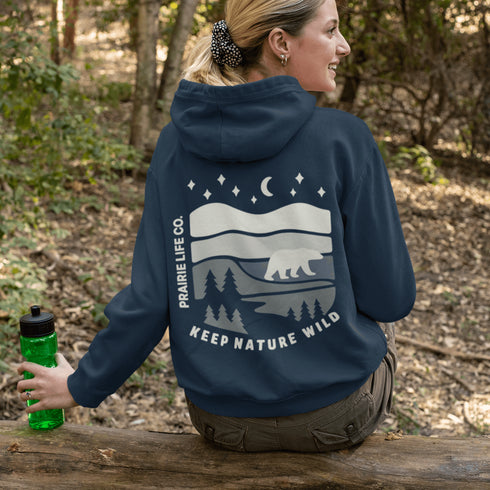 This design features a minimalist polar bear silhouette, gracefully wandering across layered prairie hills, framed by dense pine forests and a serene night sky.