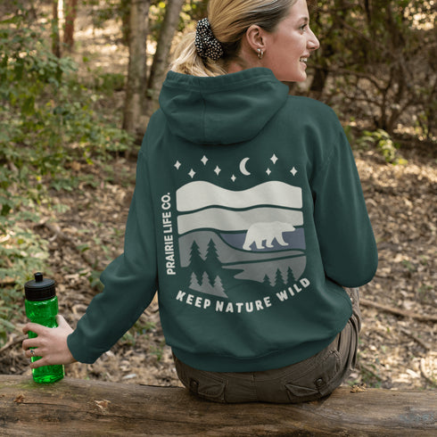 This design features a minimalist polar bear silhouette, gracefully wandering across layered prairie hills, framed by dense pine forests and a serene night sky.