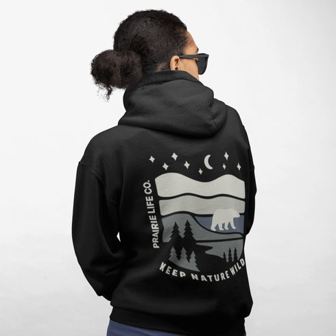 This design features a minimalist polar bear silhouette, gracefully wandering across layered prairie hills, framed by dense pine forests and a serene night sky.