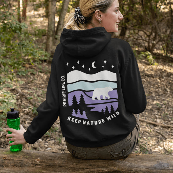 Featuring a sleek polar bear silhouette wandering through layered frozen prairie hills, this hoodie design evokes the serenity of untouched nature.