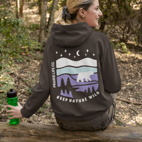 Featuring a sleek polar bear silhouette wandering through layered frozen prairie hills, this hoodie design evokes the serenity of untouched nature.