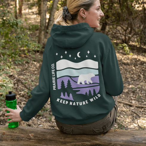 Featuring a sleek polar bear silhouette wandering through layered frozen prairie hills, this hoodie design evokes the serenity of untouched nature.