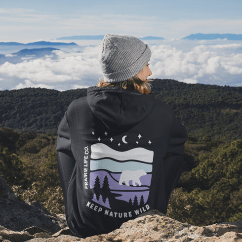Featuring a sleek polar bear silhouette wandering through layered frozen prairie hills, this hoodie design evokes the serenity of untouched nature.