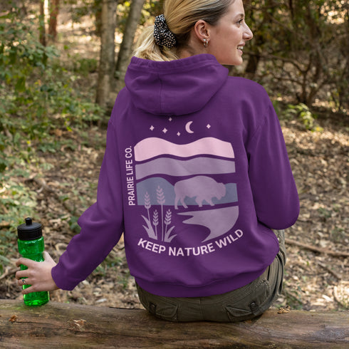 The hoodie showcases a bison standing above wheat with an open prairie sky, blending modern style with the wild spirit of the Canadian countryside.