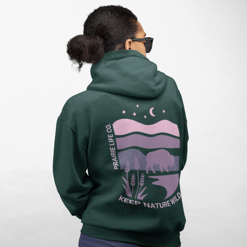 The hoodie showcases a bison standing above wheat with an open prairie sky, blending modern style with the wild spirit of the Canadian countryside.