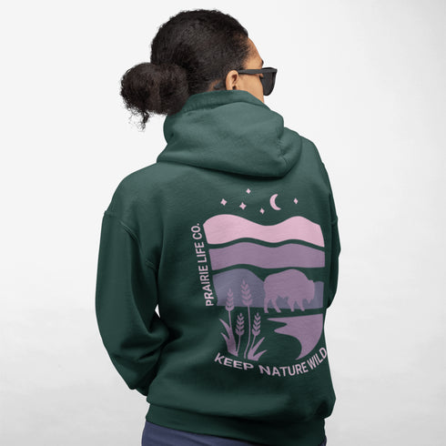The hoodie showcases a bison standing above wheat with an open prairie sky, blending modern style with the wild spirit of the Canadian countryside.