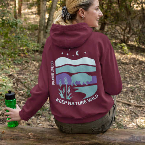 This hoodie features a color-blocked design in pastel blue and purple hues. The graphic showcases a powerful bison standing above wheat with an open prairie sky