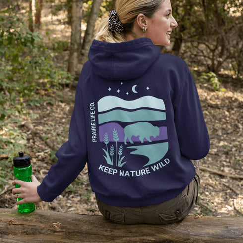 This hoodie features a color-blocked design in pastel blue and purple hues. The graphic showcases a powerful bison standing above wheat with an open prairie sky