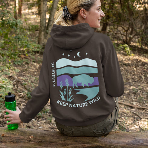 This hoodie features a color-blocked design in pastel blue and purple hues. The graphic showcases a powerful bison standing above wheat with an open prairie sky