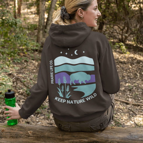 This hoodie features a color-blocked design in pastel blue and purple hues. The graphic showcases a powerful bison standing above wheat with an open prairie sky