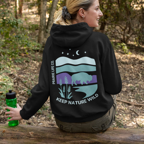 This hoodie features a color-blocked design in pastel blue and purple hues. The graphic showcases a powerful bison standing above wheat with an open prairie sky