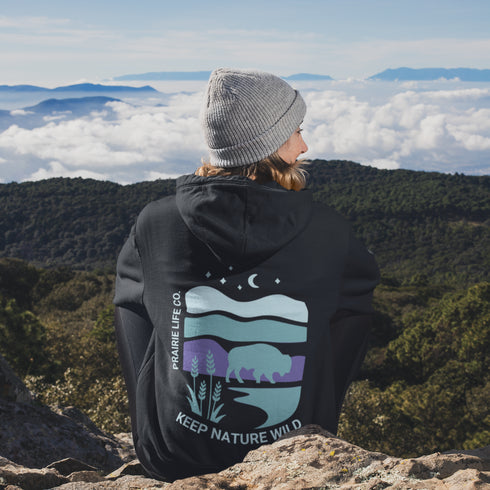 This hoodie features a color-blocked design in pastel blue and purple hues. The graphic showcases a powerful bison standing above wheat with an open prairie sky