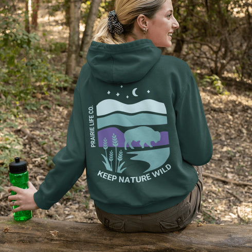 This hoodie features a color-blocked design in pastel blue and purple hues. The graphic showcases a powerful bison standing above wheat with an open prairie sky