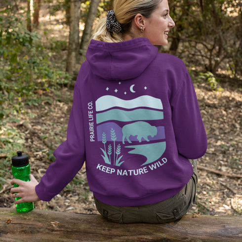 This hoodie features a color-blocked design in pastel blue and purple hues. The graphic showcases a powerful bison standing above wheat with an open prairie sky