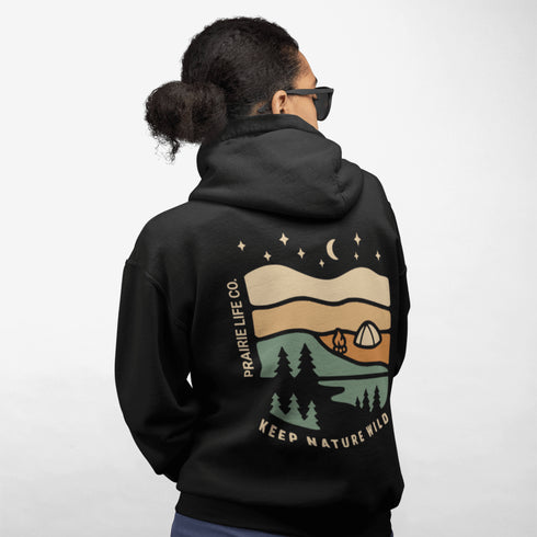 This hoodie features rolling prairie hills, a glowing campfire beside a cozy tent, towering pines, and a star-filled night sky complete with a crescent moon.