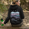 This hoodie features a nature graphic showcasing prairie hills, pine trees, a cozy tent, and a glowing campfire under a crescent moon and star-filled sky.