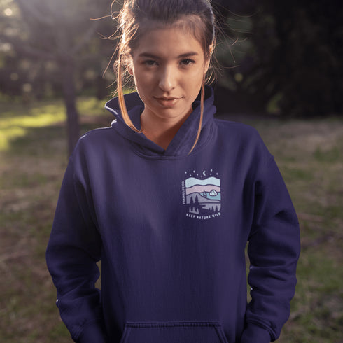 This hoodie features a nature graphic showcasing prairie hills, pine trees, a cozy tent, and a glowing campfire under a crescent moon and star-filled sky.