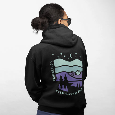 This hoodie features a retro-style landscape graphic with prairie hills, pine trees, a campfire, a tent, and a night sky filled with stars and a crescent moon.
