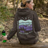 This hoodie features a retro-style landscape graphic with prairie hills, pine trees, a campfire, a tent, and a night sky filled with stars and a crescent moon.