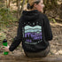 This hoodie features a retro-style landscape graphic with prairie hills, pine trees, a campfire, a tent, and a night sky filled with stars and a crescent moon.