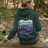 This hoodie features a retro-style landscape graphic with prairie hills, pine trees, a campfire, a tent, and a night sky filled with stars and a crescent moon.