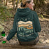 This hoodie features rolling prairie hills, a glowing campfire beside a cozy tent, towering pines, and a star-filled night sky complete with a crescent moon.