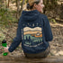 This hoodie features rolling prairie hills, a glowing campfire beside a cozy tent, towering pines, and a star-filled night sky complete with a crescent moon.