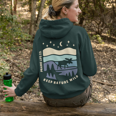 This hoodie features a moose silhouette roaming across prairie hills, pine trees with stars scattered above and a crescent moon glowing softly.