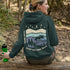 This hoodie features a moose silhouette roaming across prairie hills, pine trees with stars scattered above and a crescent moon glowing softly.