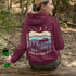 This hoodie features a moose silhouette roaming across prairie hills, pine trees with stars scattered above and a crescent moon glowing softly.