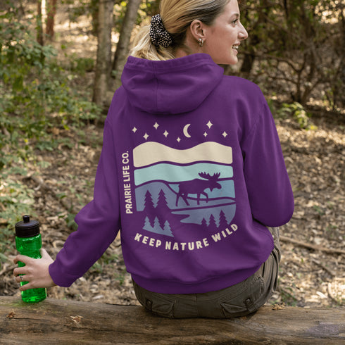 This hoodie features a moose silhouette roaming across prairie hills, pine trees with stars scattered above and a crescent moon glowing softly.