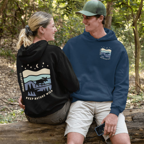 This hoodie features a moose silhouette roaming across prairie hills, pine trees with stars scattered above and a crescent moon glowing softly.